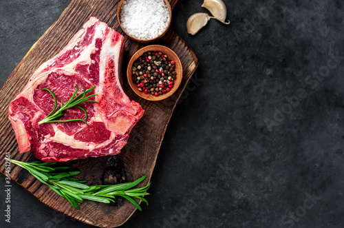 Raw cowboy steak. Marbled beef meat with spices on a stone background