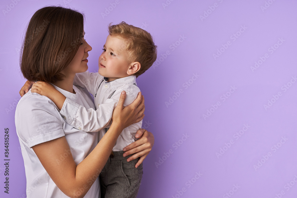portrait of sweet caucasian child boy with mother isolated over purple background. young mom and kid hugging, boy looks at mom with love