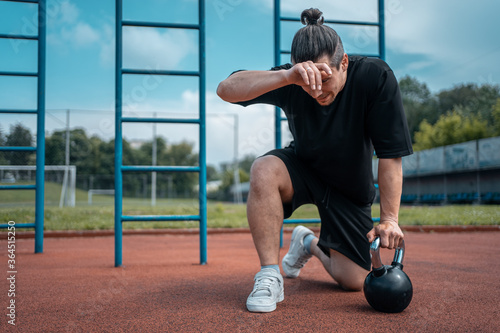 exhausted man athlete taking break between exercising with kettlebell outdoor
