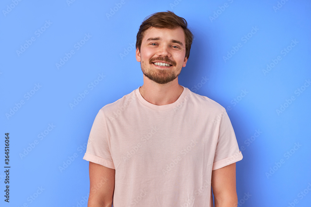 portrait of smiling guy isolated over blue background. handsome bearded male in casual t-shirt looks at camera, open-minded portrait of smiling guy isolated over blue background. handsome bearded male in casual t-shirt looks at camera, open-minded