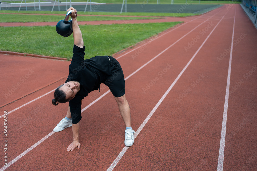 young athlete has workout and doing sport exercises with kettlebell outdoor