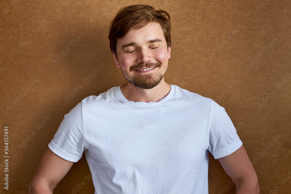 shy calm male with closed eyes, smile at camera after joke. have fun, isolated brown background