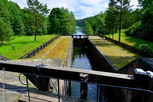 Close up on massive dam doors used to lower or increase water level with a narrow channel with concrete edges seen in the middle of a dense forest or moor on a cloudy summer day in Poland