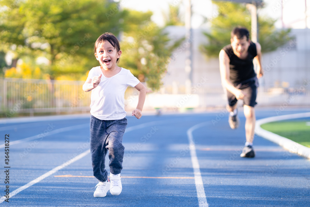 Asian little daughter is running in the stadium together with father, concept of outdoor activity, sport, exercise and competition learning for kid development.