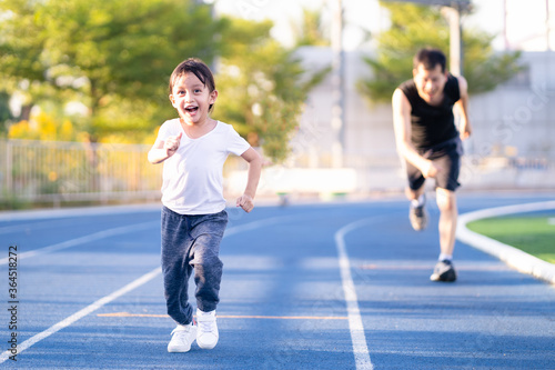 Asian little daughter is running in the stadium together with father, concept of outdoor activity, sport, exercise and competition learning for kid development.