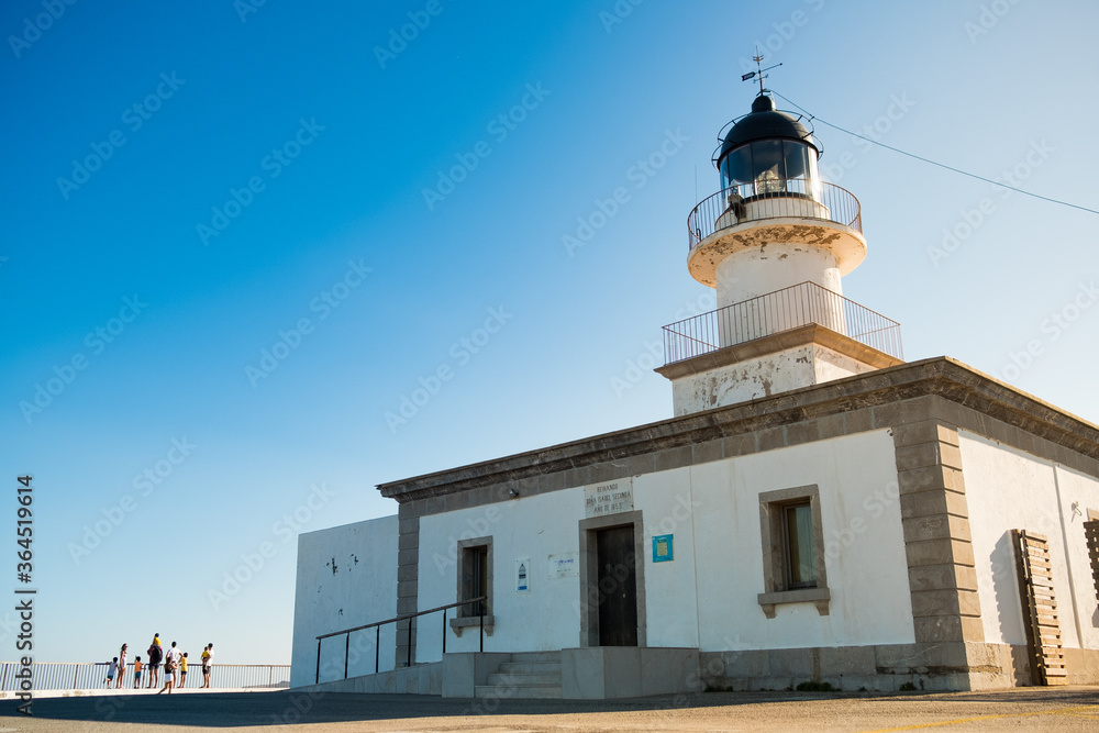 view of cap de creus lighthouse, a beacon of light on the rocky catalan costa brava, on a sunny summer day at sunset with warm light and wind blowing