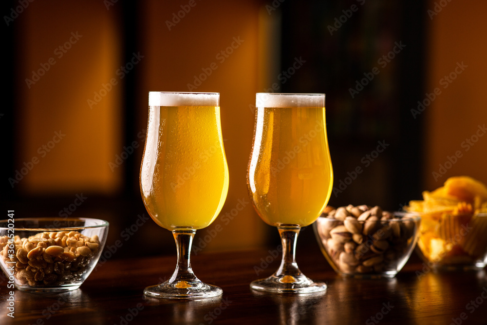 Crispy snacks for client. Two glasses of light beer and chips and nuts on bar Crispy snacks for client. Two glasses of light beer and chips and nuts on bar