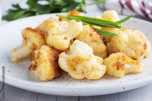 Fried cauliflower florets in batter on a white plate. White wooden background.