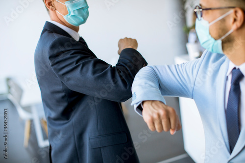 Two colleagues avoid a handshake when meeting in the office and greet with bumping elbows photo