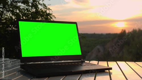 Black laptop with a green screen is on a folding table at sunset at top of mountain.