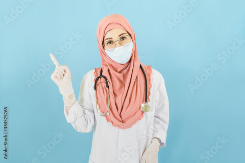 Smart young muslim woman doctor in lab coat with Medical face mask,white latex medical gloves and stethoscope against blue background,health care concept