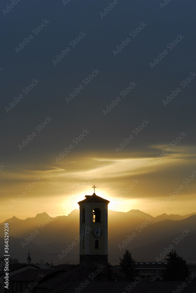 Sunset between mountains and dark clouds behind bell tower silhouette with clock Sunset between mountains and dark clouds behind bell tower silhouette with clock
