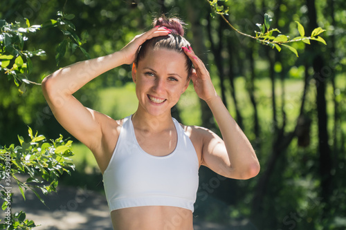 Portrait of a young beautiful pumped-up girl in the park with collected hair in a sporty white top