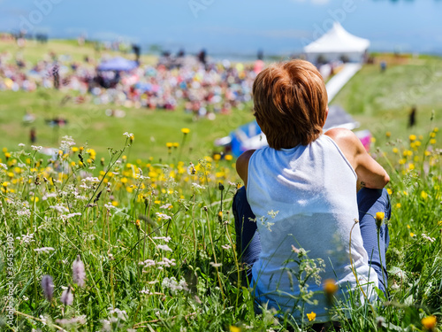 Elderly woman sitting in a meadow listens to a music concert. photo