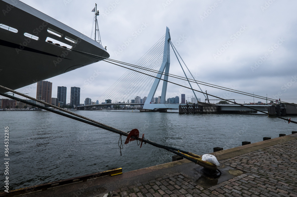Skyline of Rotterdam with Erasmus Bridge and in the foreground a ship that is attached to the quay on a cloudy day