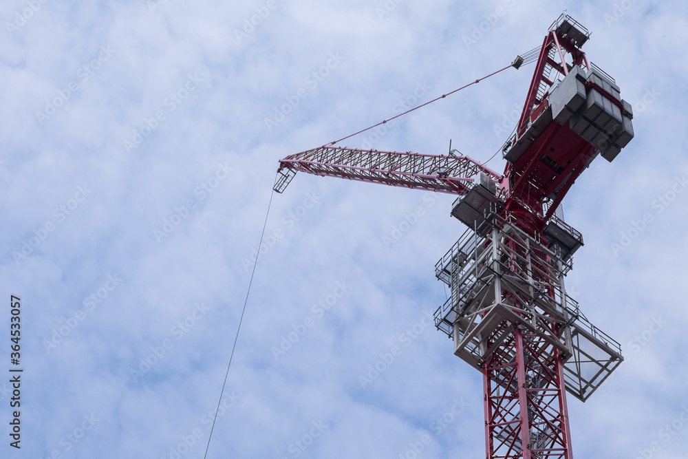 Very high hoisting crane used for building skyscrapers against a cloudy blue sky Very high hoisting crane used for building skyscrapers against a cloudy blue sky