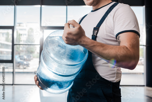 cropped view of delivery man holding heavy gallon with water photo