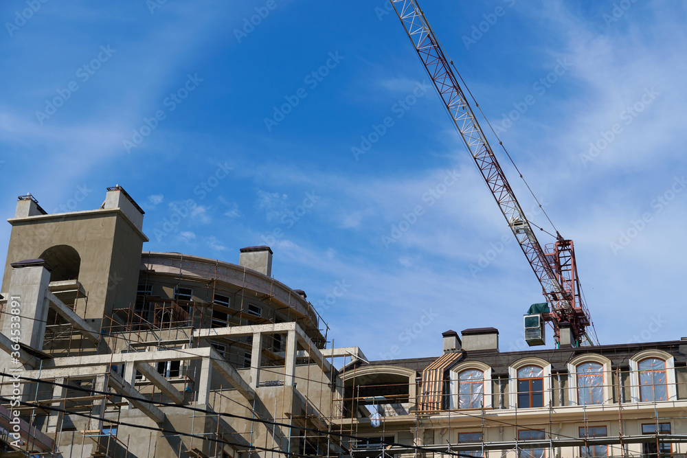 Fototapeta premium modern building under construction, plastered walls and scaffolding, construction crane
