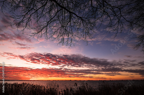 View in winter with beautiful rising sun on the village of Oosterzee on the other side of Lake Tjeukemeer in the province of Friesland in the Netherlands photo