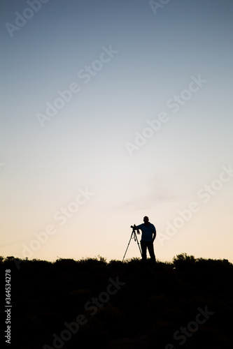 Silhouette of a photographer with his tripod on a hill with dawn setting in.