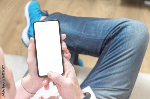 mockup cellphone. Man sitting on a sofa and holding a blank screen mobile phone.