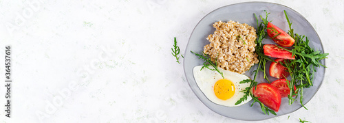 Breakfast oatmeal porridge with fried egg, tomatoes, arugula. Healthy food. Top view, overhead, banner