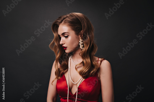 Wallpaper Mural Attractive woman in red top posing on black background. Sad curly lady in satin dress looks down on isolated backdrop Torontodigital.ca