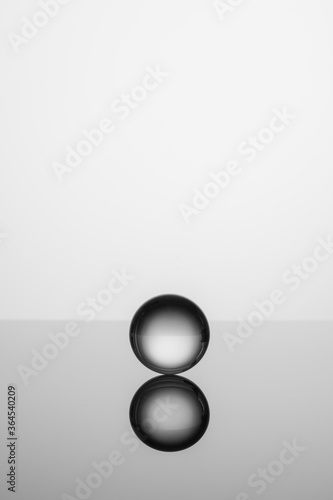 Clear transparent crystal glass ball isolated on studio background with reflection on the surface. Black and white photo