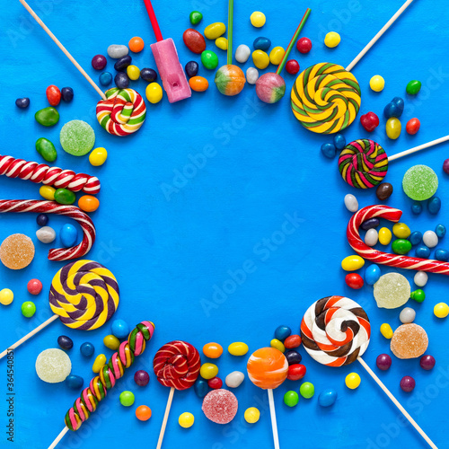 Colored candies, lollipops and marmalade on a blue background round frame. Top view, flat lay.