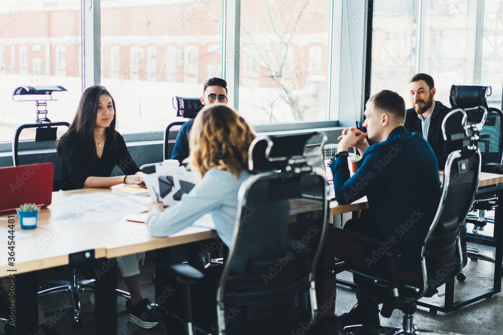 Business meeting of young male and female entrepreneurs dressed in formal wear in modern office interior.Employees sitting at meeting table during conference with proud ceo in finance company Business meeting of young male and female entrepreneurs dressed in formal wear in modern office interior.Employees sitting at meeting table during conference with proud ceo in finance company