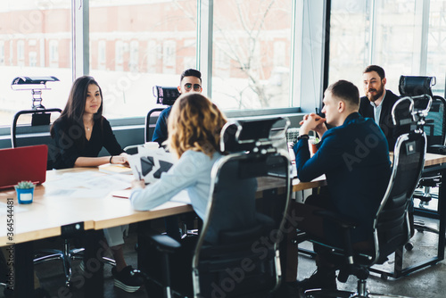 Business meeting of young male and female entrepreneurs dressed in formal wear in modern office interior.Employees sitting at meeting table during conference with proud ceo in finance company