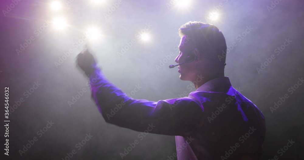 Man stand up comedian speaking jokes in micropphone standing on stage, side view. Funny performance, concert. Guy showman entertains audience under the light, front view. Actor plays role in theatre. Man stand up comedian speaking jokes in micropphone standing on stage, side view. Funny performance, concert. Guy showman entertains audience under the light, front view. Actor plays role in theatre.
