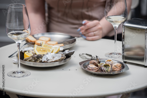 oysters and snails with a glass of wine are served on a plate in a cafe. cooked oysters and snails on a table in a cafe