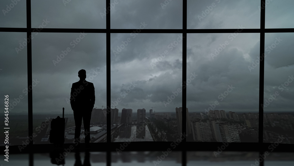 Fototapeta premium The man with suitcase standing near the big windows in the business center