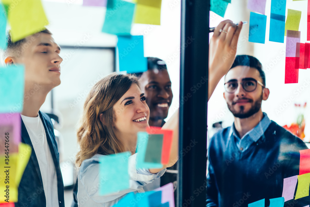 © BullRun - Diverse team of positive young people laughing while working together during brainstorming and standing behind glass wall with sticky colorful papers.Cheerful students learning words from stickers © BullRun - Diverse team of positive young people laughing while working together during brainstorming and standing behind glass wall with sticky colorful papers.Cheerful students learning words from stickers