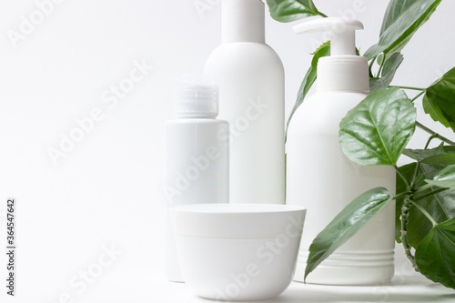 Set of cosmetic cans of organic cosmetics for face and body care on a white background with green leaves. Cream  shampoo and lotion on a light background. Layout  copy space.