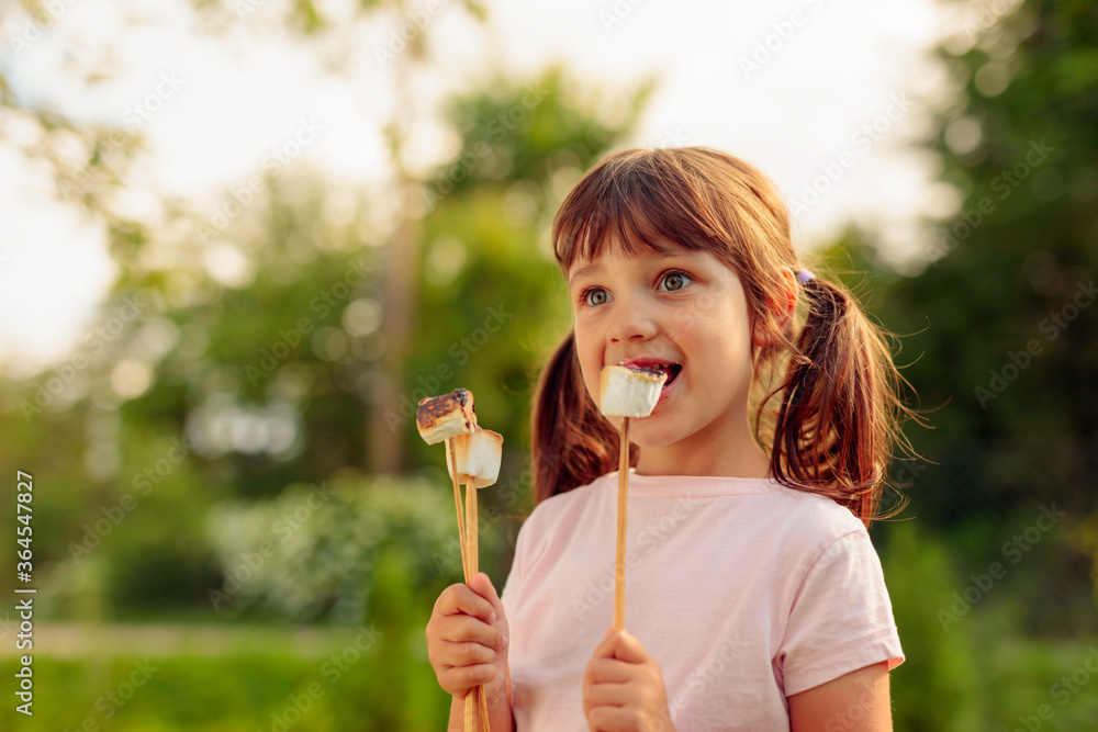 Four-year-old girl eats marshmallows toasted over a fire. Four-year-old girl eats marshmallows toasted over a fire.