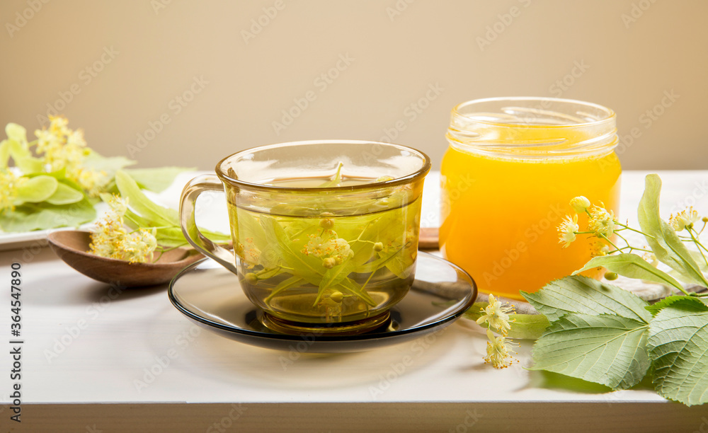 Tilia platyphyllos known as large-leaved linden herbal tea with freshly picked blossoms and jar of honey with tree leaves and branches with blossoms for decoration on wood table. Tilia platyphyllos known as large-leaved linden herbal tea with freshly picked blossoms and jar of honey with tree leaves and branches with blossoms for decoration on wood table.