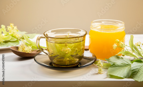 Tilia platyphyllos known as large-leaved linden herbal tea with freshly picked blossoms and jar of honey with tree leaves and branches with blossoms for decoration on wood table.