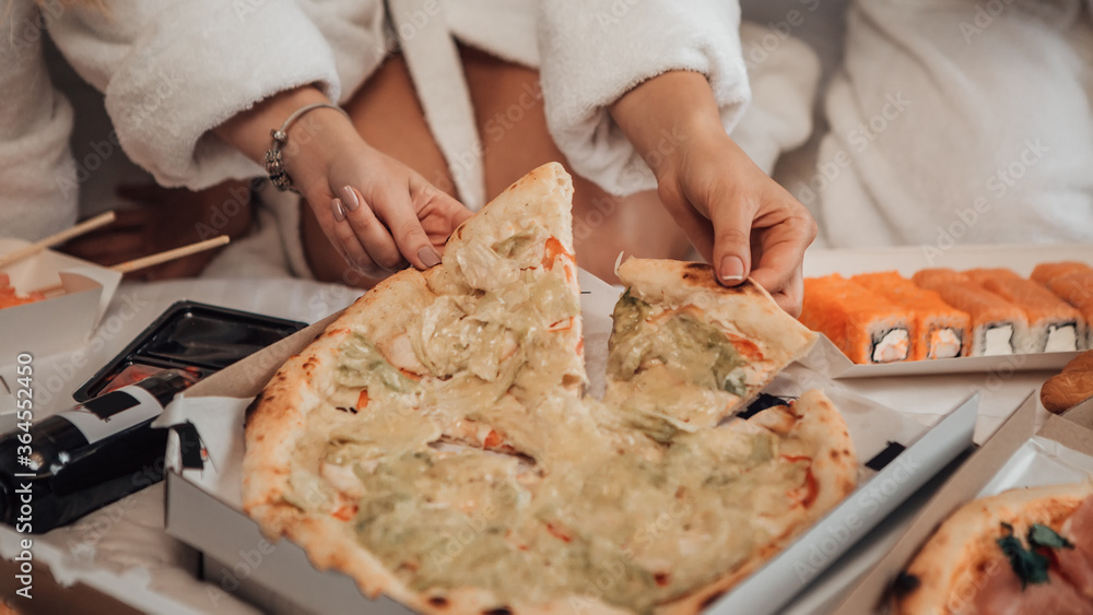 Pizza party! Close up shot of girls hands reaching for a slice of pizza. Latin american female have a birthday in luxury hotel room. Sushi set, Italian and French food delivery in corona virus.