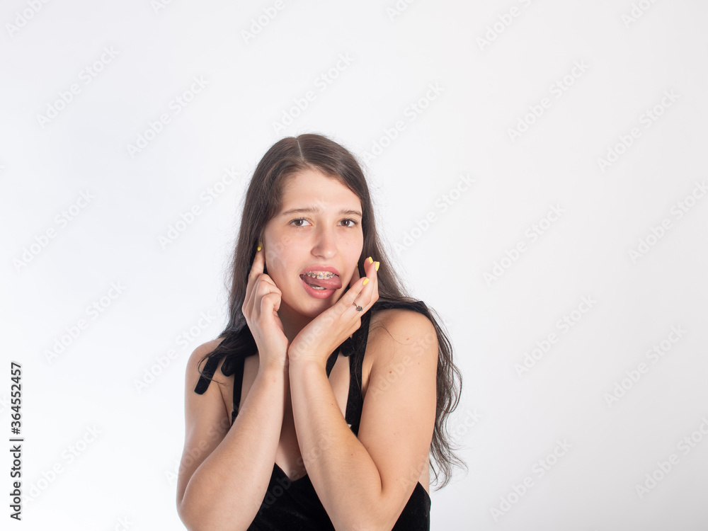 Portrait of a young black-haired girl with braces on her teeth on a white background. girl flirting with her tongue hanging out isolate on a white background. space for text. Portrait of a young black-haired girl with braces on her teeth on a white background. girl flirting with her tongue hanging out isolate on a white background. space for text.