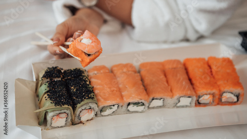 Close up shot of assorted sushi set with shrimps on bed served on eco friendly cardboard plate. Various kinds of japanese food made from rice, raw fish and sesame. Food delivery in hotel appartments. 