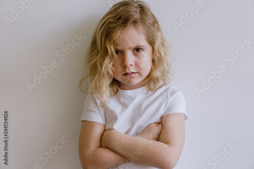 Disappointed little child in casual t shirt looking at camera on white background in studio