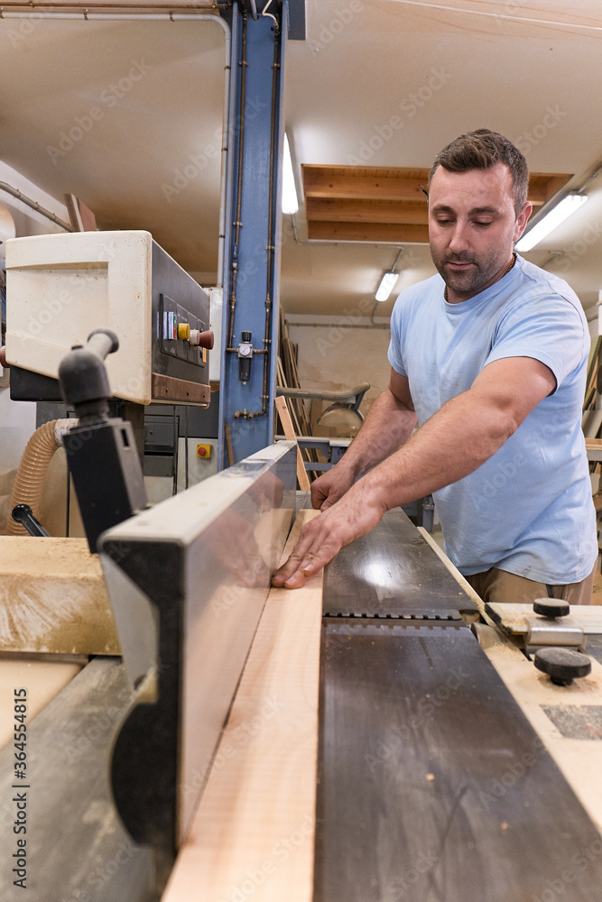 Male woodworker in casual clothes focusing and cutting lumber using special electric machine while working in light modern workshop Male woodworker in casual clothes focusing and cutting lumber using special electric machine while working in light modern workshop