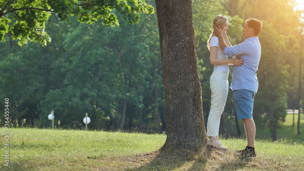 Fototapeta premium A young man and woman are standing under a tree in a park and hugging.