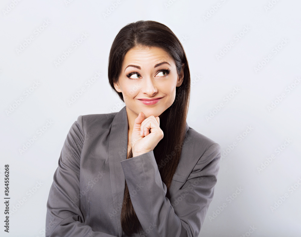 Beautiful smiling business woman in suit holding the hands under the face and looking up on blue background. Closeup Beautiful smiling business woman in suit holding the hands under the face and looking up on blue background. Closeup