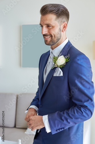 Smiling fiance in classy suit standing in bright living room of modern apartment during wedding fees
