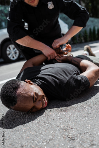 Selective focus of detained African American man lying on ground near policeman with handcuffs, racism concept © LIGHTFIELD STUDIOS
