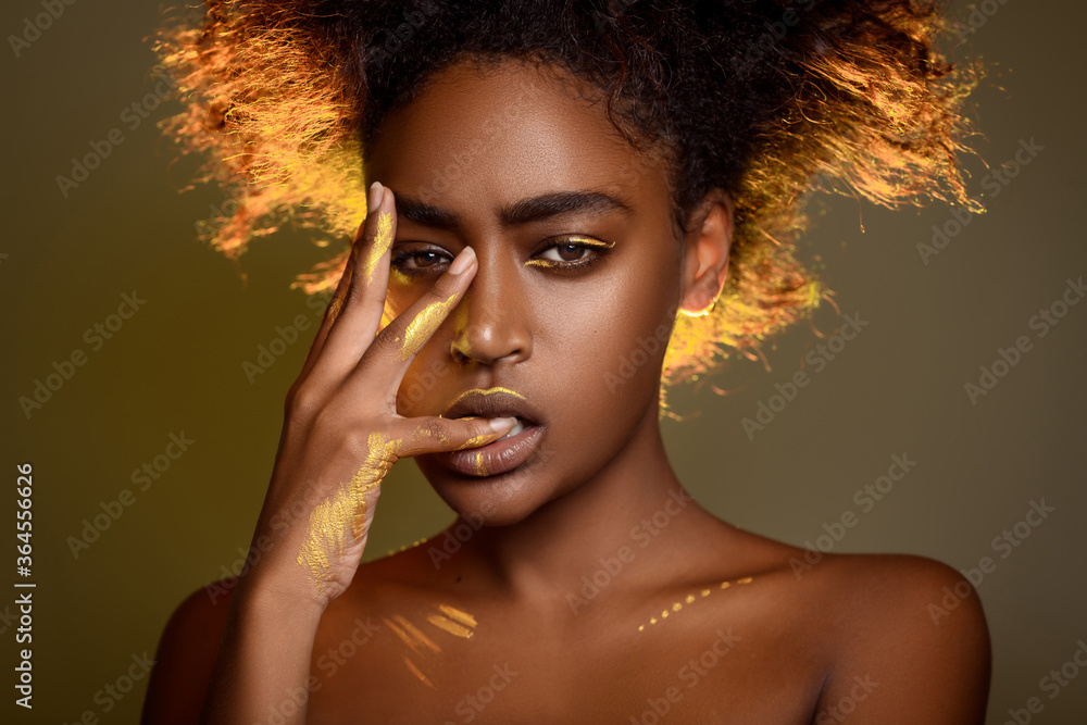 Portrait of a sensual african woman with gold paint on her face and hands. She bit her fingers. Ethnic fashion and style. Portrait of a sensual african woman with gold paint on her face and hands. She bit her fingers. Ethnic fashion and style.