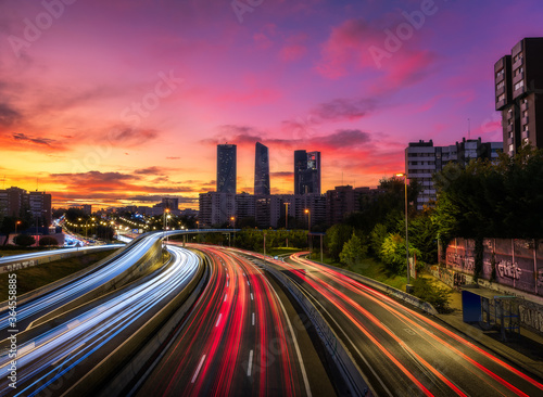 Drone view of cityscape with luminous highway in long exposure and skyscrapers under sunset sky photo